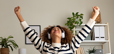 Woman sitting on a couch with a laptop and headset, joyfully raising her hands